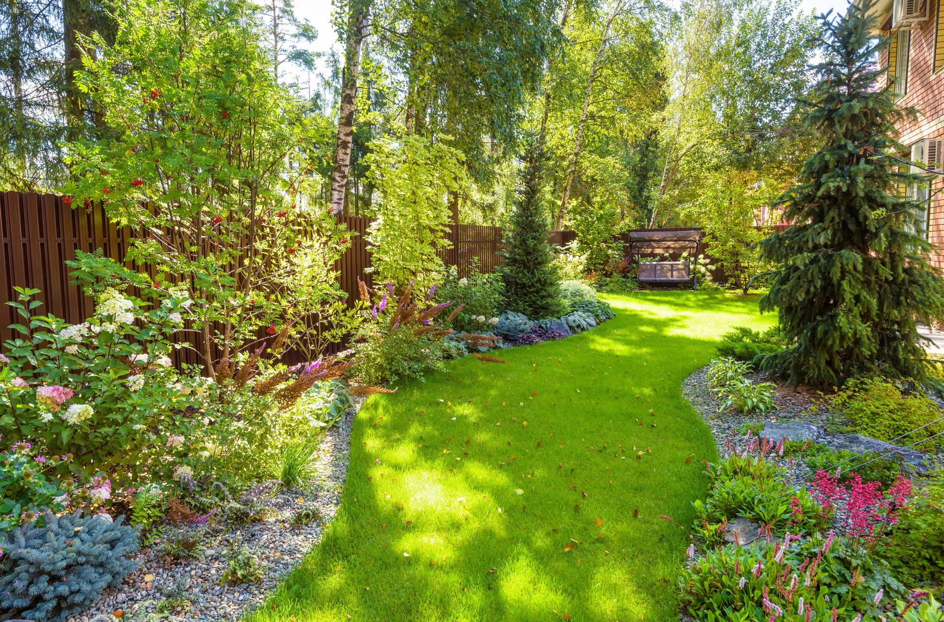 Landschaftsgestaltung im grünen Hausgarten. Landschaftsgestaltung mit Pflanzen und Blumen im Wohnhaus. Malerische Aussicht auf schönen angelegten Garten im Hinterhof.